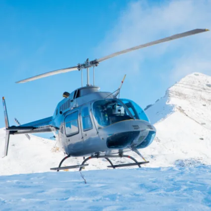 A helicopter parked on a snowfield below a mountain ridge.