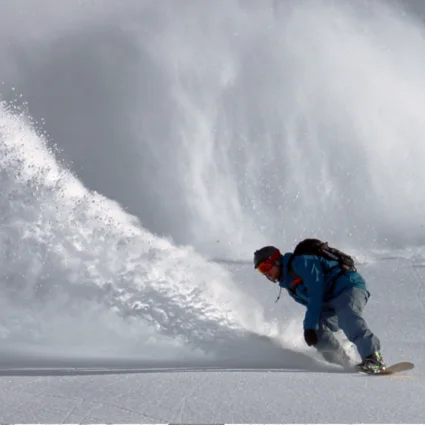 A snowboarder throwing a wall of powder out of a deep off-piste turn.