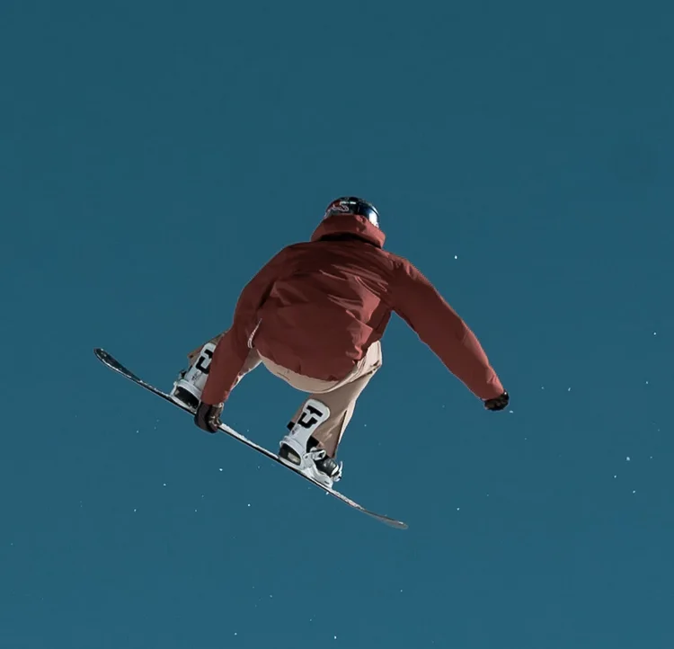 A snowboarder grabbing the board high above the slope against a deep blue sky.