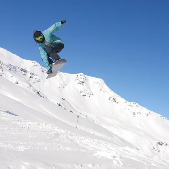 A snowboarder grabbing the board mid-air off a snowpark kicker against a blue sky.