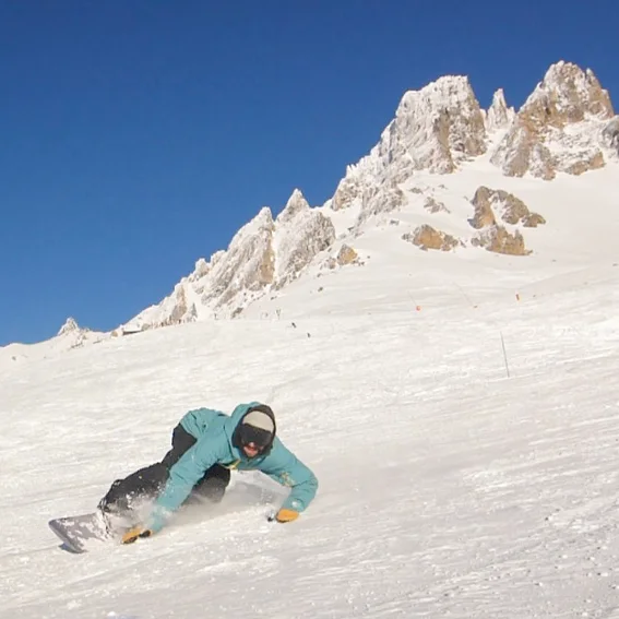 A rider laying a low toeside carve below a rocky summit.