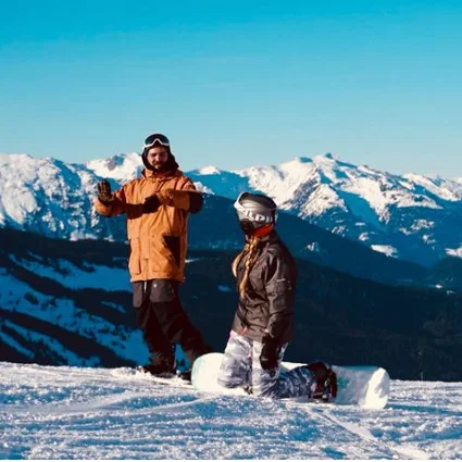 An instructor coaching a rider sitting on their board at the top of a run.