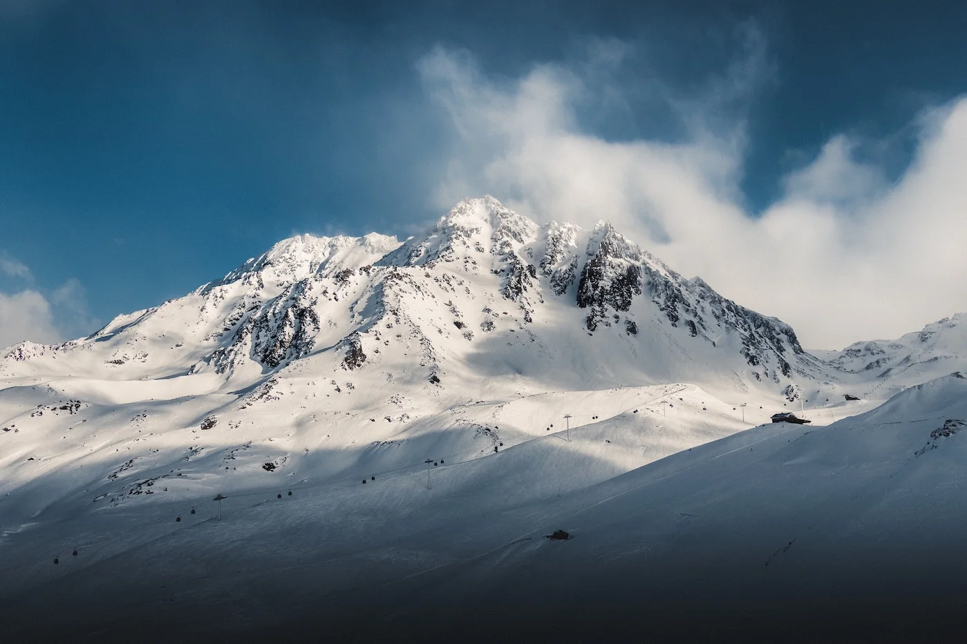 Snow-covered peaks above Val Thorens with cloud spilling over the summit ridge.