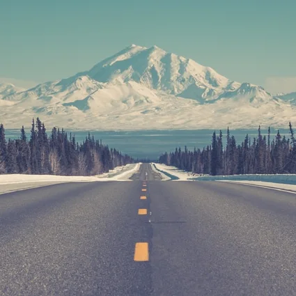 An empty mountain road running straight towards a snow-capped peak.